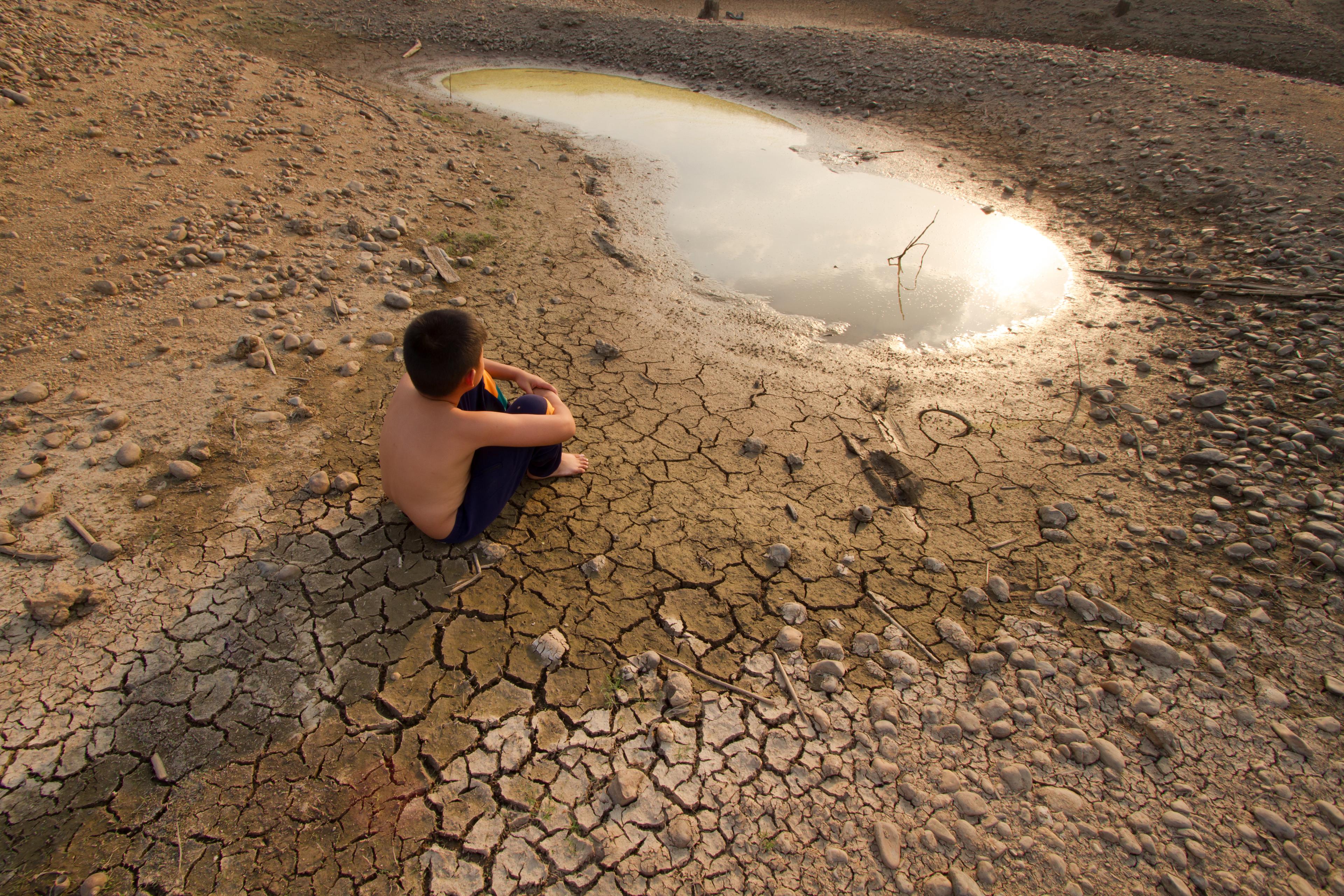 Watercrisis, kind zit op uitgedroogde aarde naast een klein poeltje water