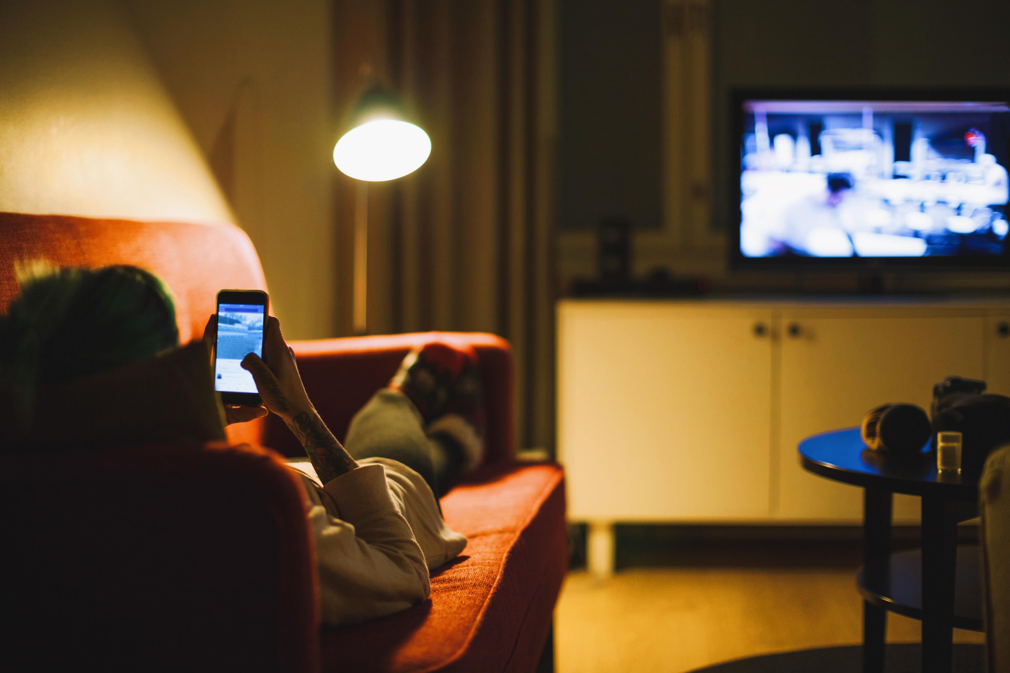 Vrouw op haar telefoon voor de televisie