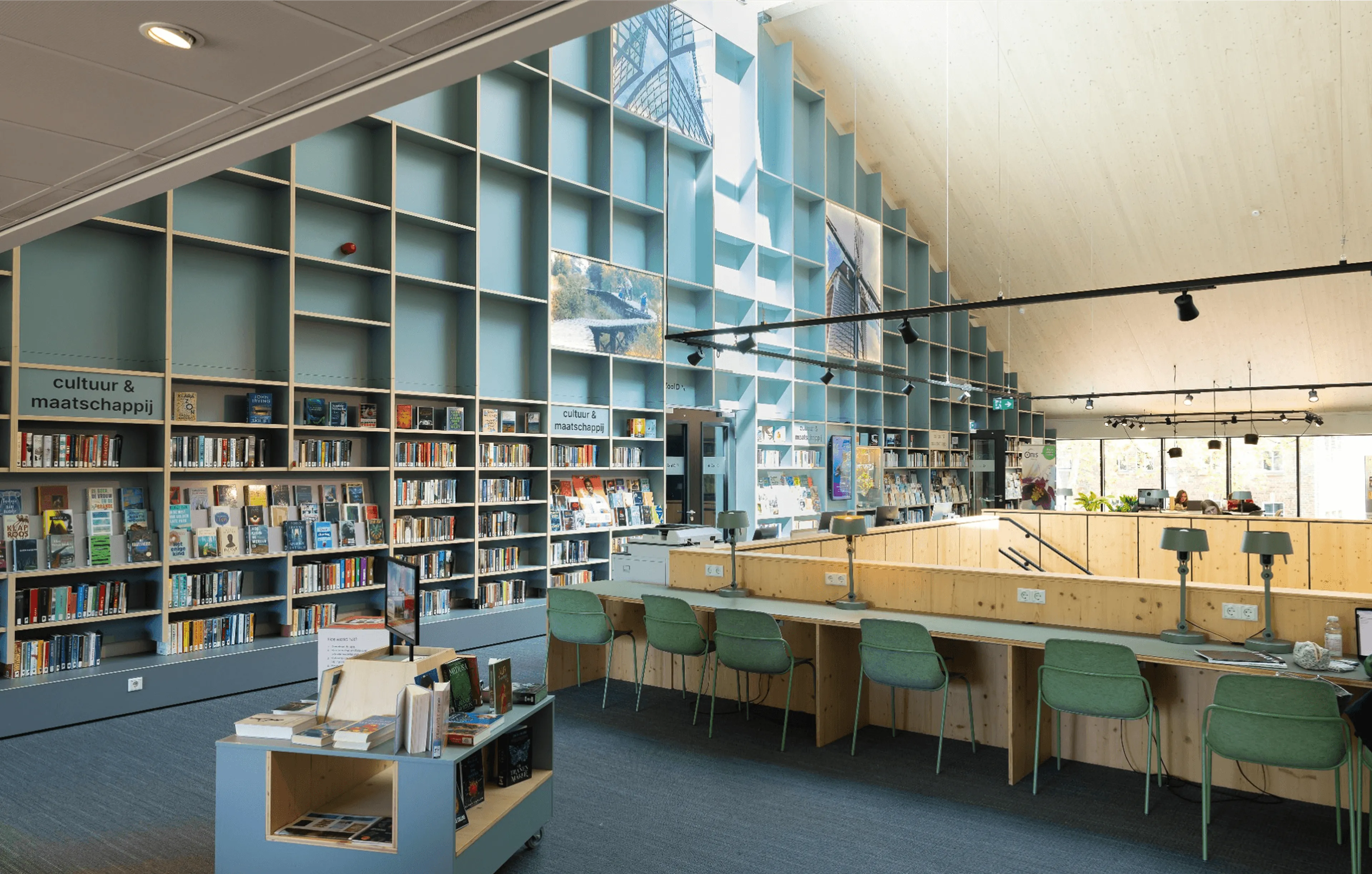 Hoge zeegroene boekenwand met houten werkbank, groene stoelen en tafellampen in 't Kwartier