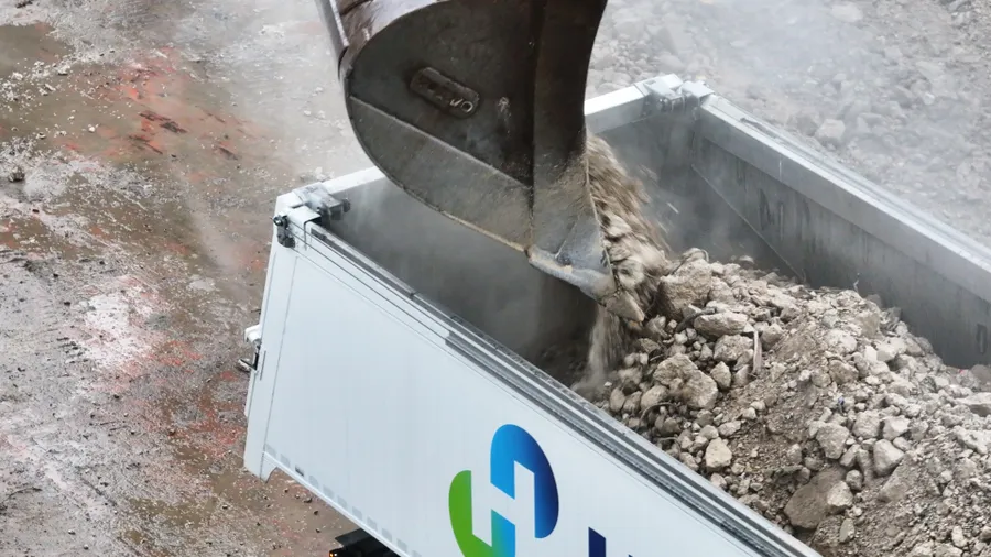 An excavator bucket loads crushed concrete into a container.