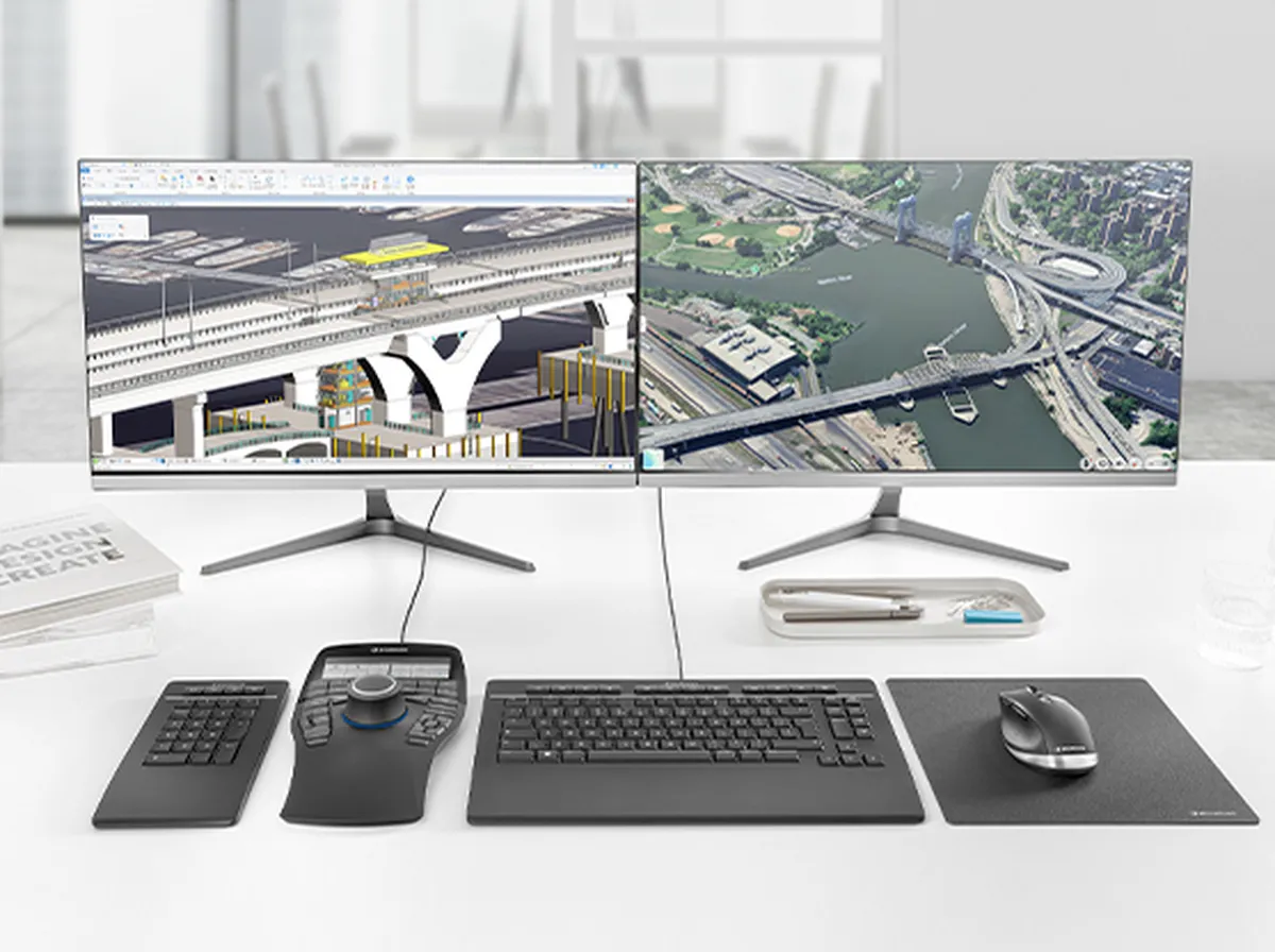 Zwei Monitore zeigen Bau- und Stadtpläne. Auf dem Tisch sind Tastatur, Maus, Eingabegerät und Stifte platziert. Modulares modernes Büro-Setup.