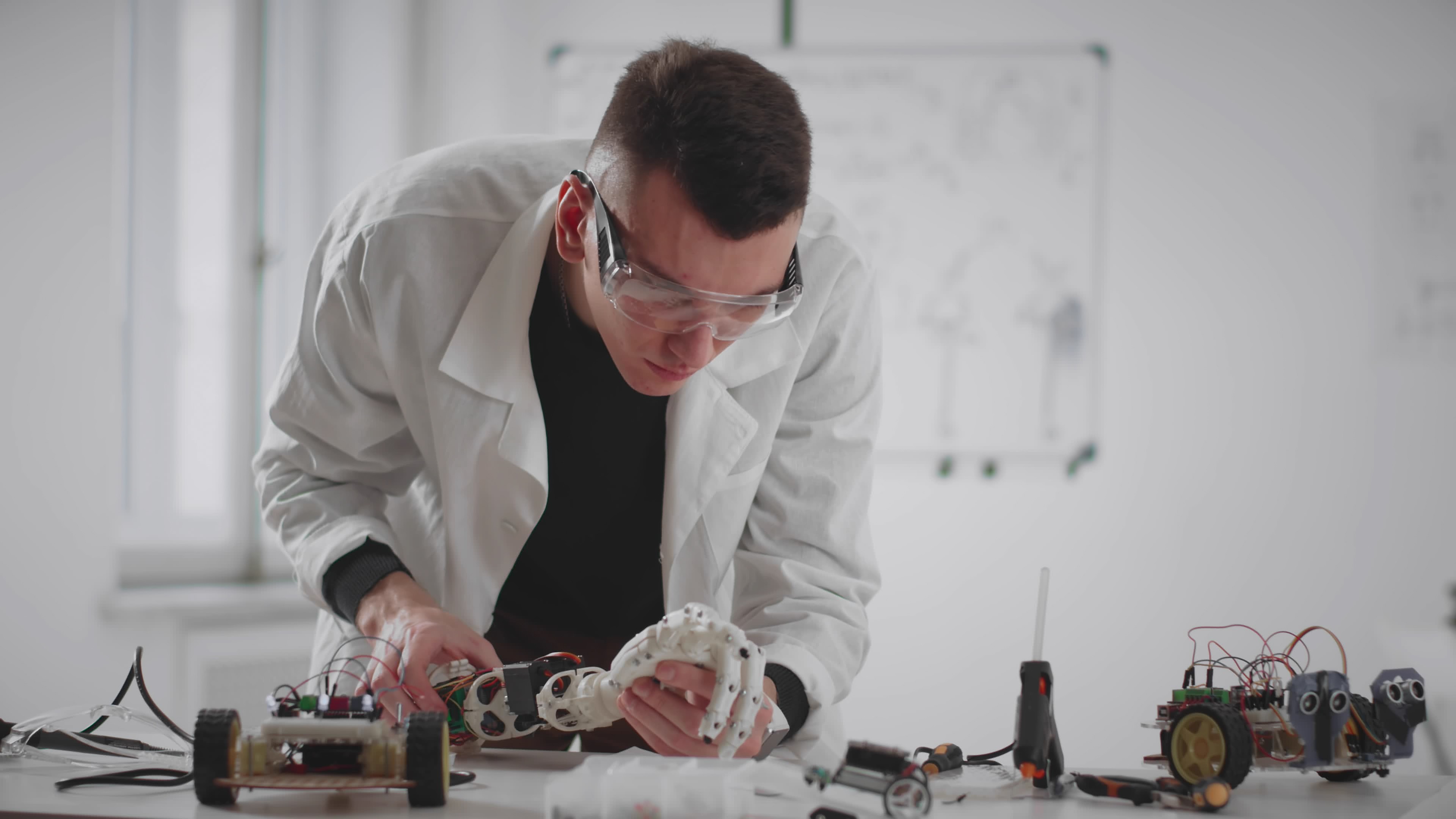 An engineer works on a robotic hand at a lab workbench.