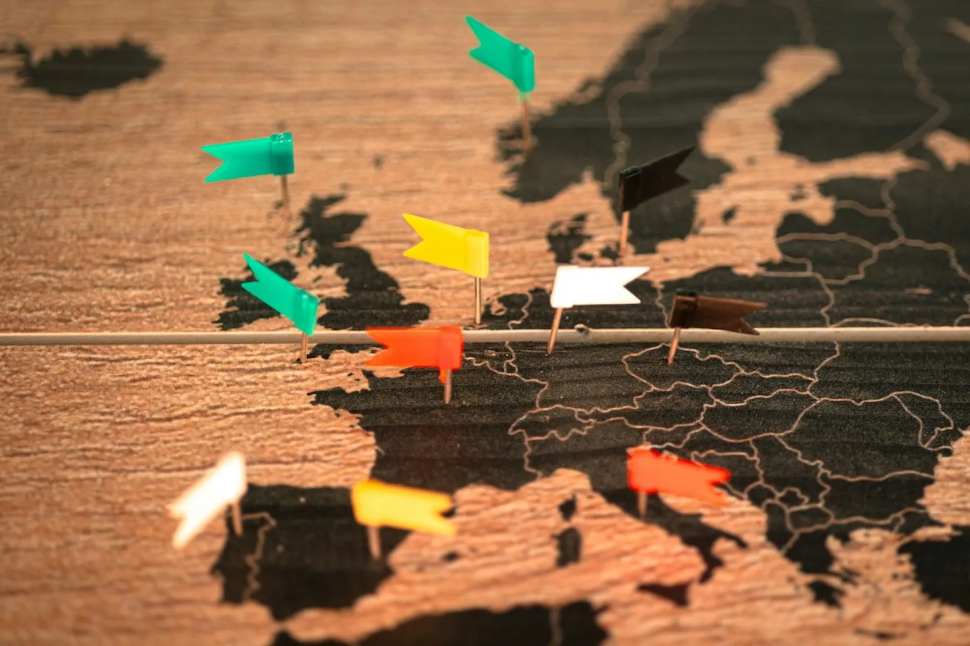 Coloured flag pins across a wooden map of Europe