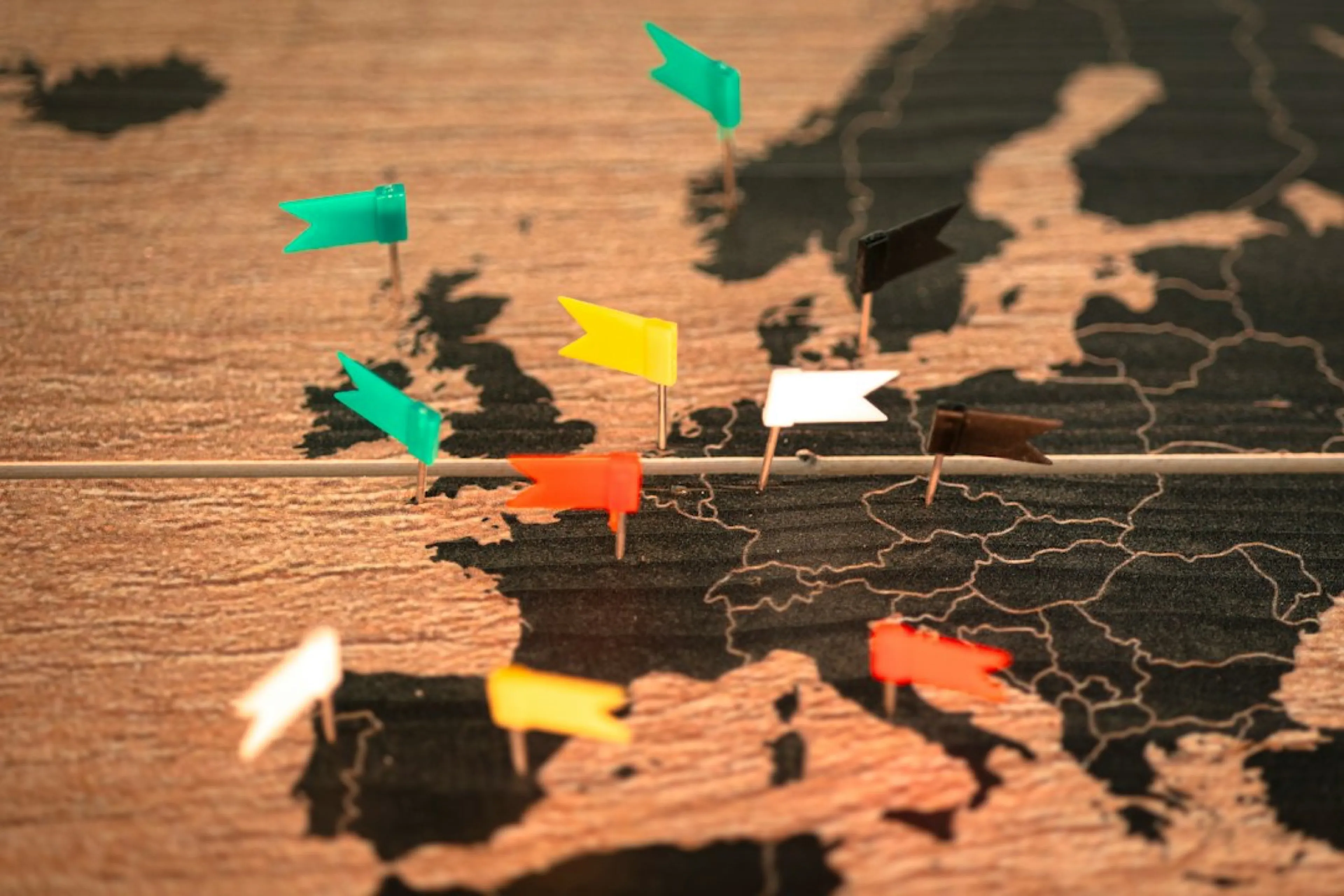 Coloured flag pins across a wooden map of Europe