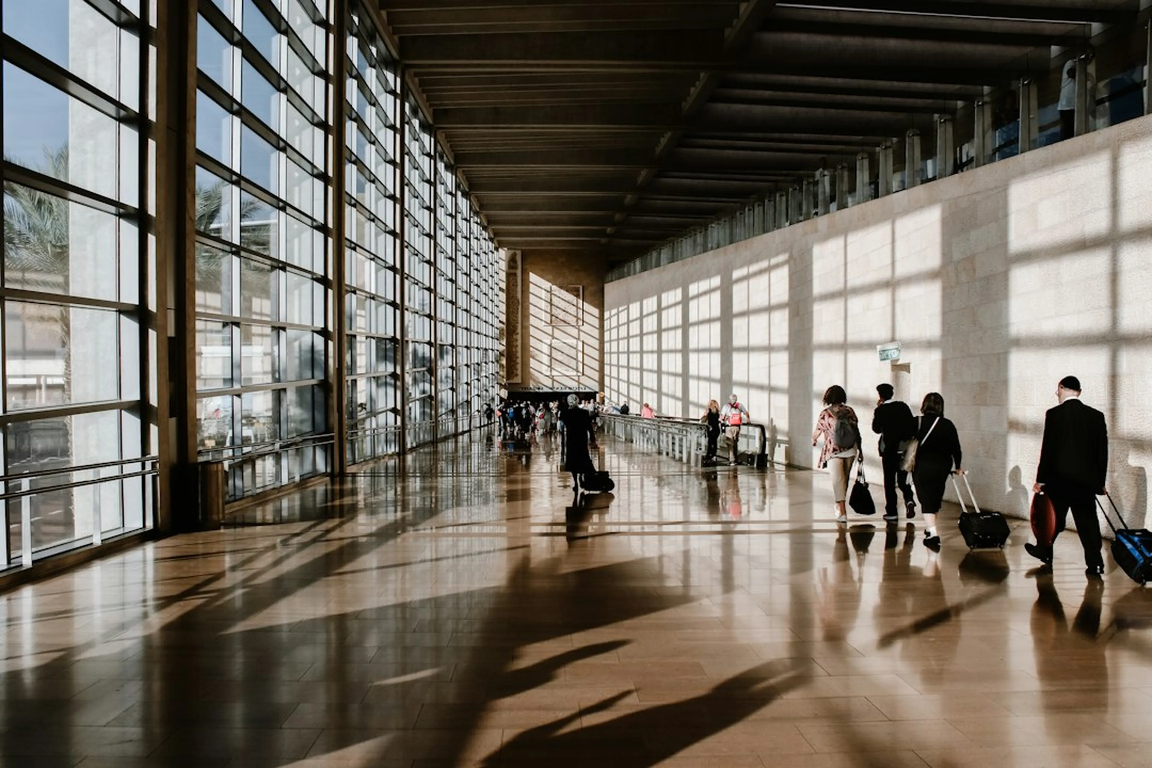 Travellers with luggage walking through a sunlit airport terminal