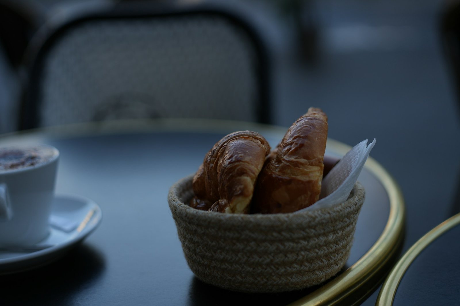 A basket of croissants beside morning coffee.