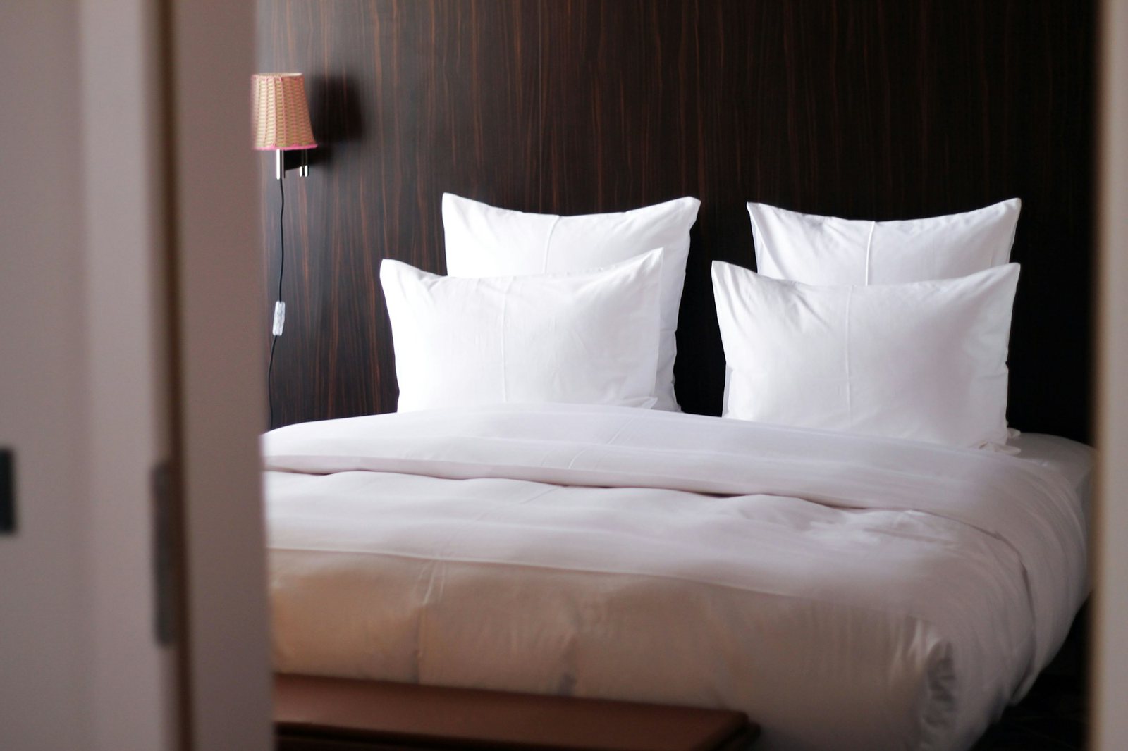 A calm guest room with white bedding seen through a dark timber doorway.