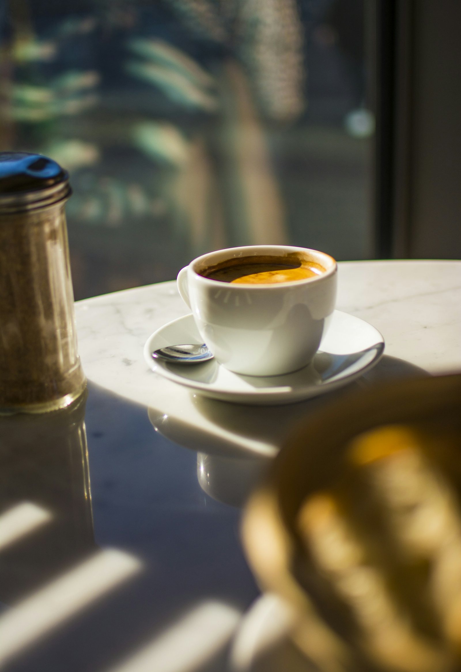 An espresso cup catching low sunlight on a marble table.