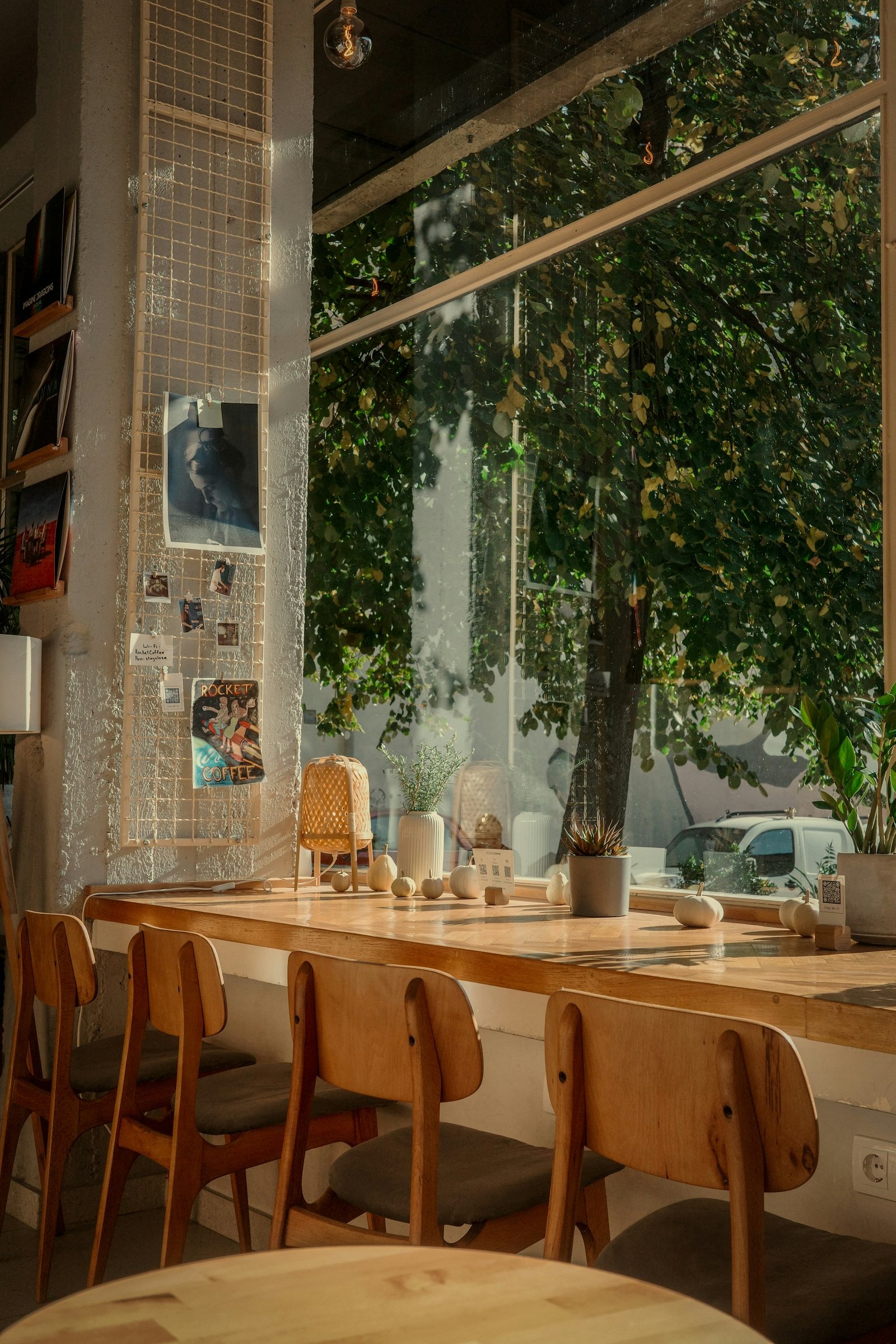 Wooden cafe tables beside a large leafy window.