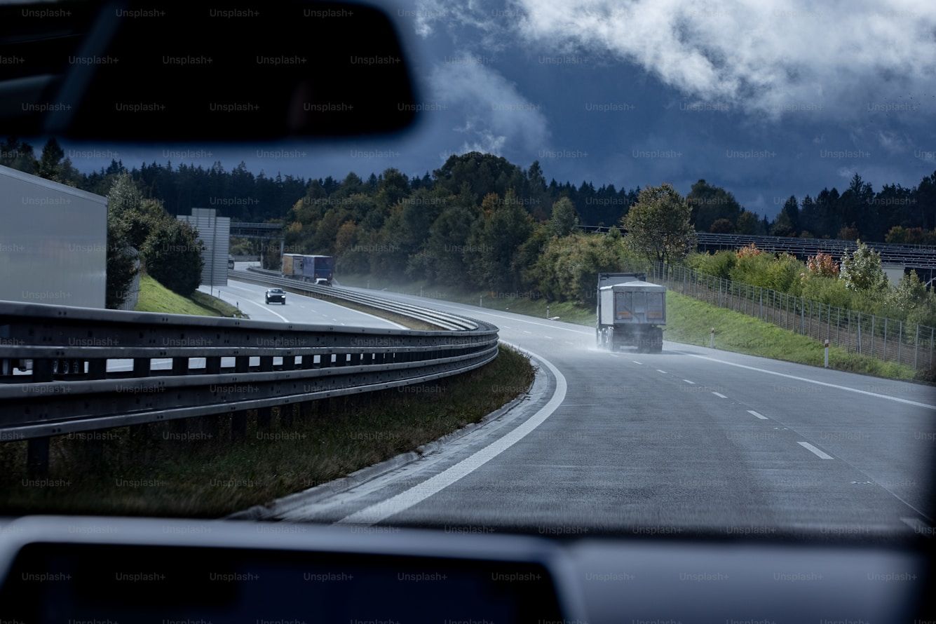 Blick aus einem Fahrzeug auf eine Autobahn mit Lastwagen zwischen bewaldeten Hängen