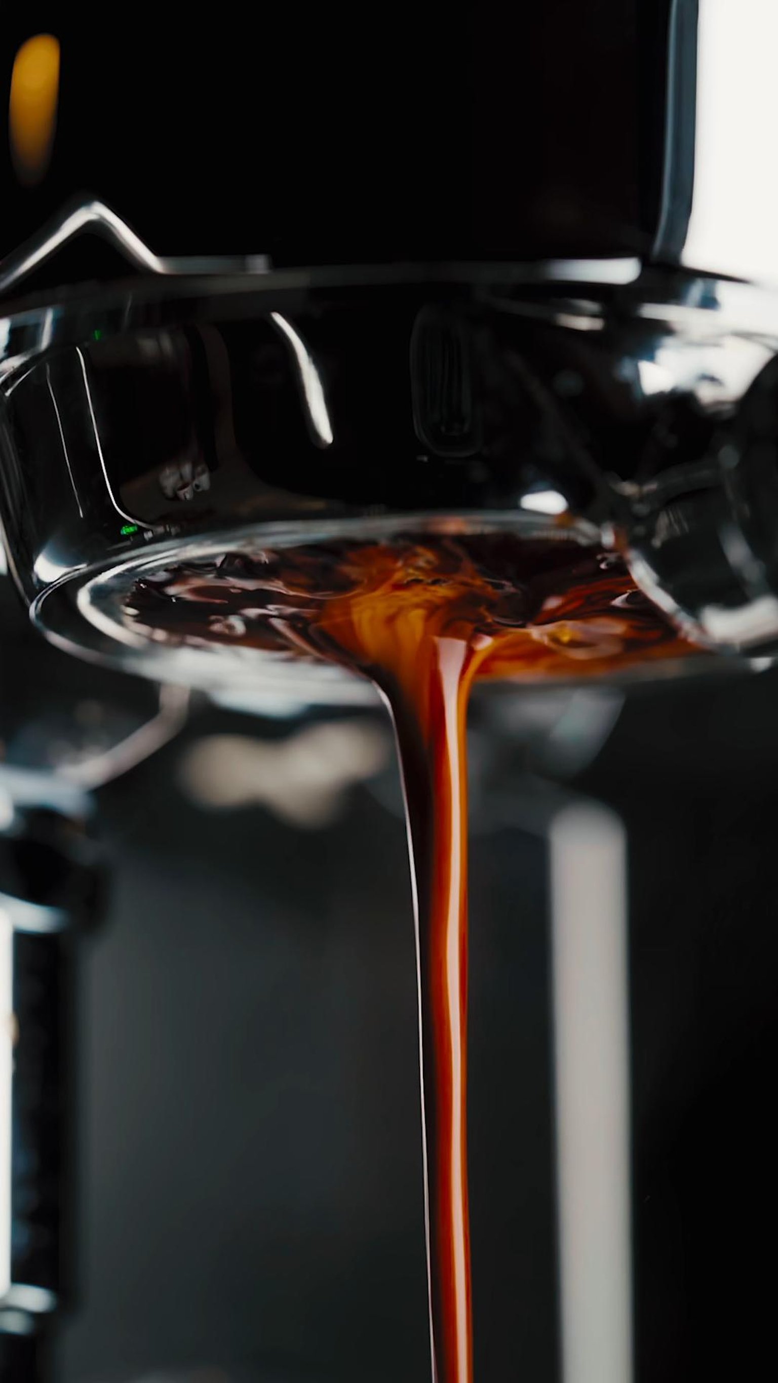 A hand uses a wooden-handled tamper on coffee grounds in a portafilter on a wooden countertop.