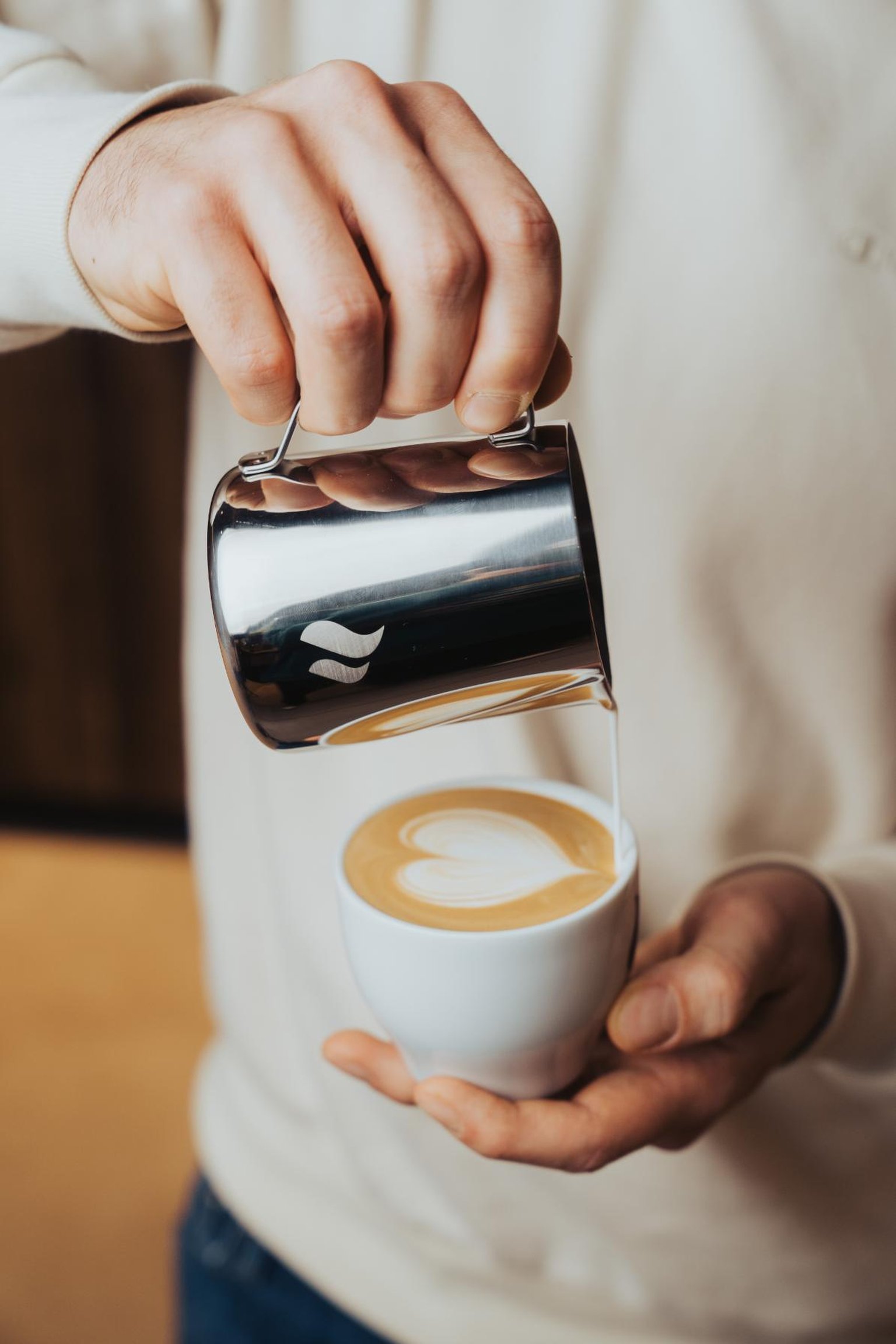 A hand uses a wooden-handled tamper on coffee grounds in a portafilter on a wooden countertop.