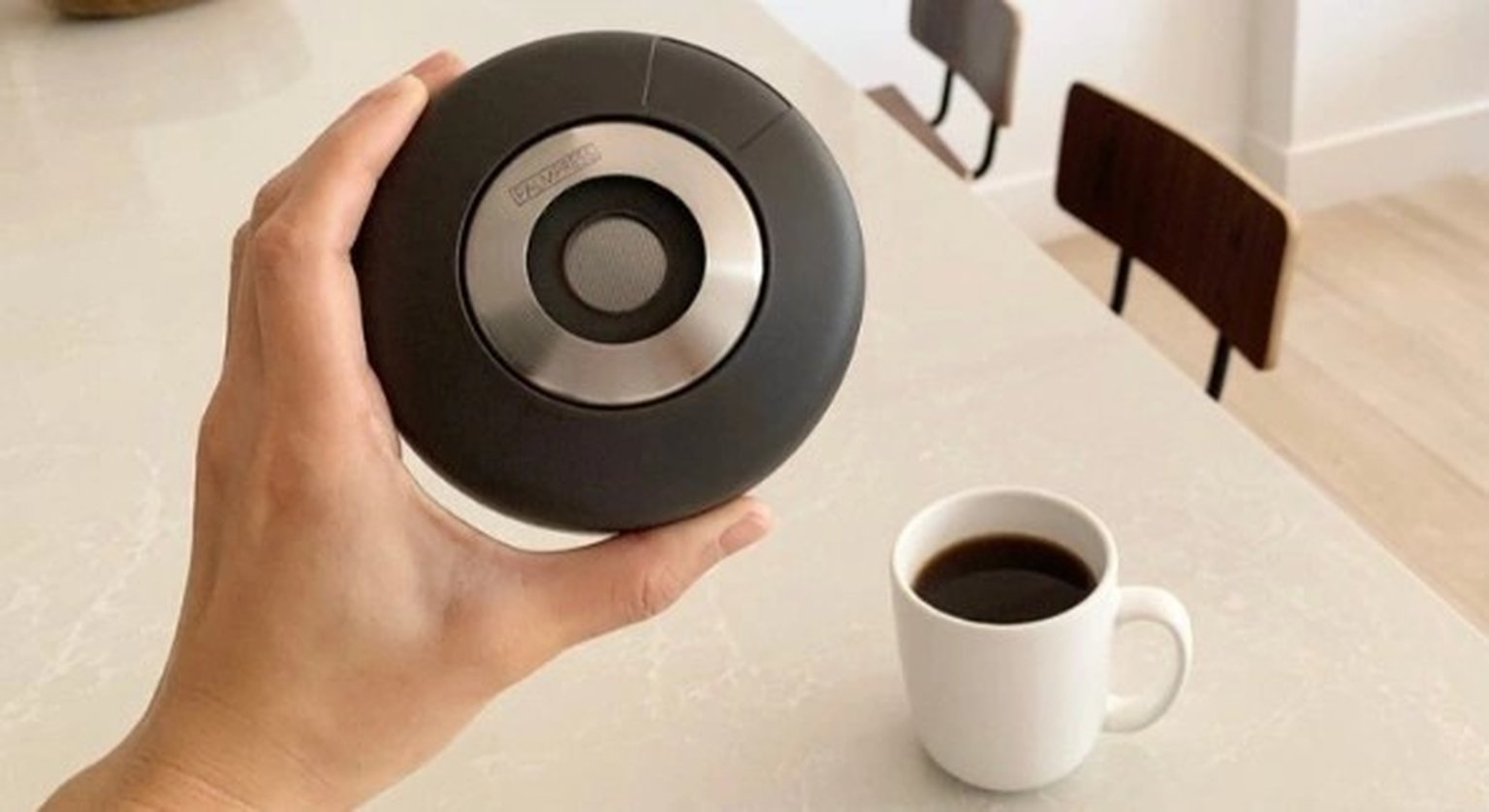 A hand uses a wooden-handled tamper on coffee grounds in a portafilter on a wooden countertop.