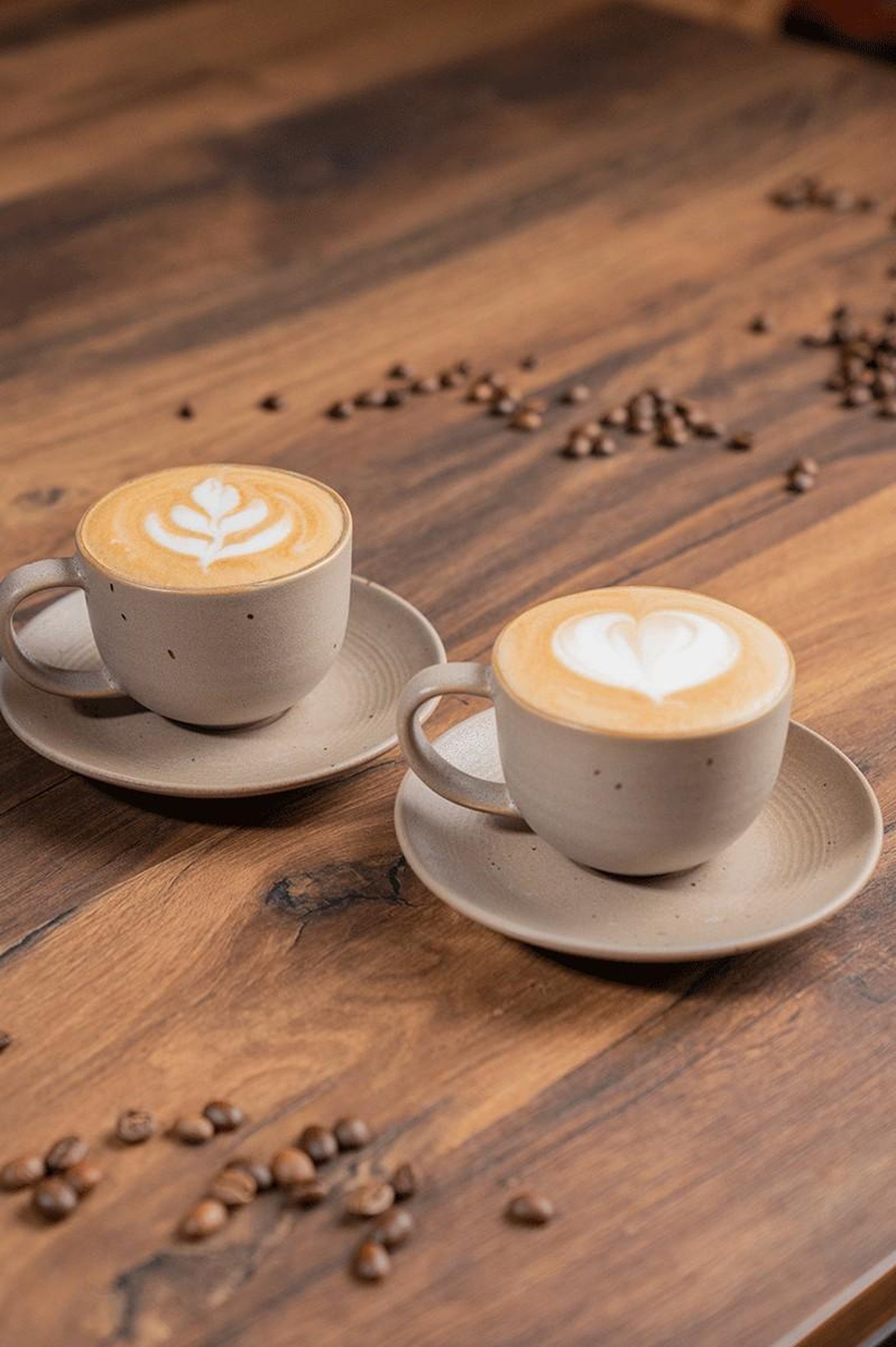 A hand uses a wooden-handled tamper on coffee grounds in a portafilter on a wooden countertop.
