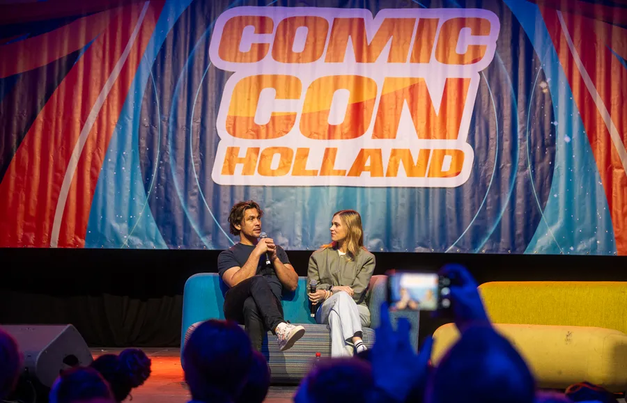 Twee panelleden spreken op het podium onder een groot Comic Con Holland-decor