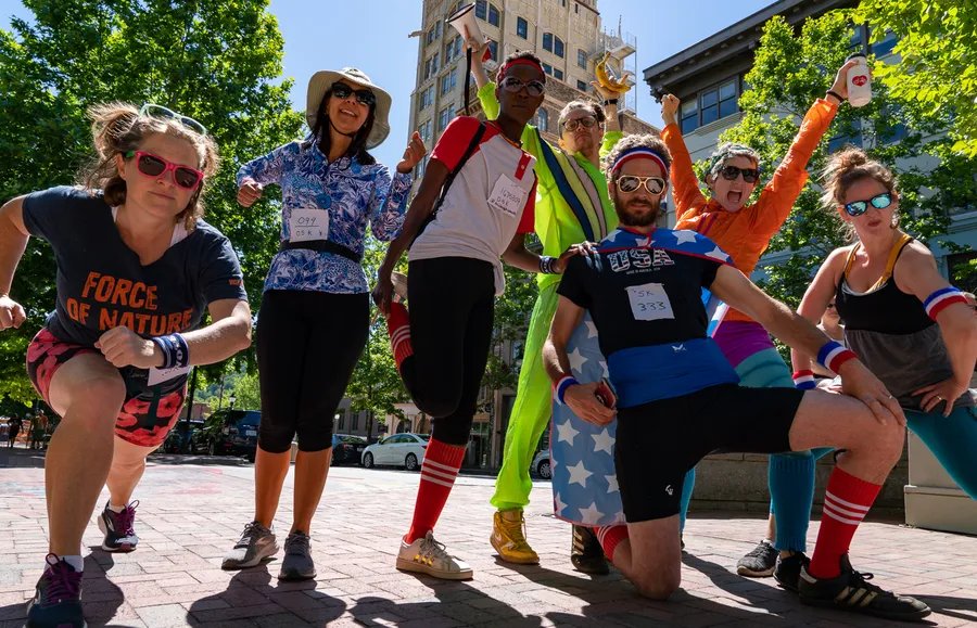 Zeven hardlopers in speelse retrokostuums poseren op een bakstenen plein voor een sponsorloop