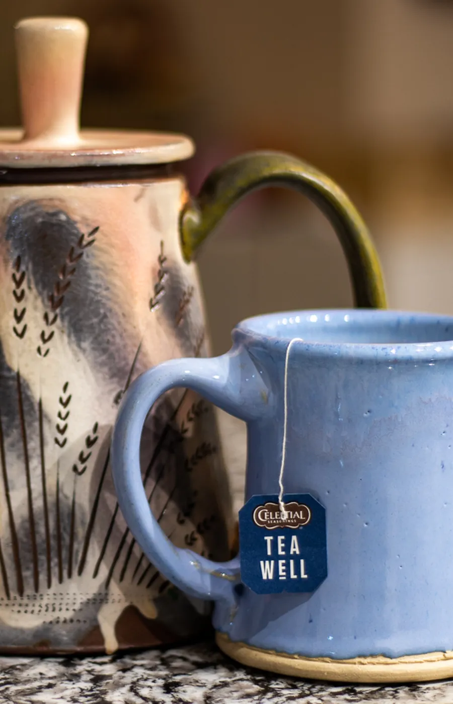 Handgemaakte keramische theepot en blauwe mok met theezakje op een granieten aanrecht
