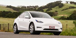 Image of a white Tesla Model Y on a rural road with green hills behind it