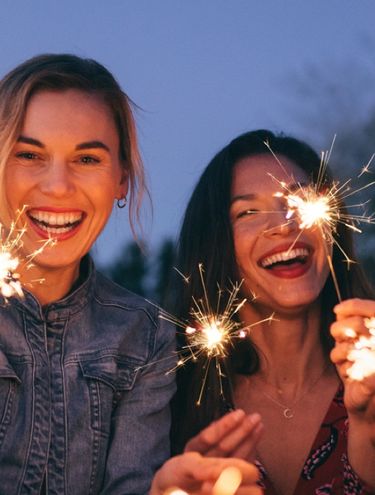 Group of friends smiling and holding sparklers at night during a celebration