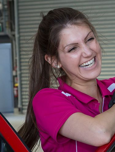 Image of a member of the GO Rentals team wearing a pink shirt smiling as she prepares a rental car for a customer
