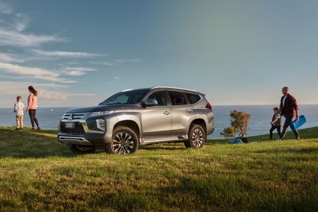Family unloading gear beside a silver 4WD parked on a grassy headland above the sea