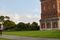 Two people walking along a path next to the historic Invercargill Water Tower, a tall red-brick structure with a domed top, set against a clear blue sky with scattered clouds