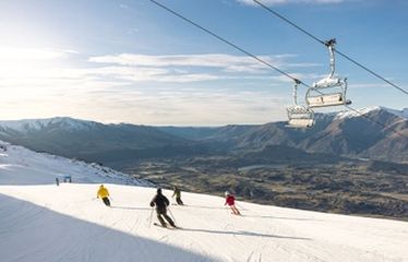 Skiers going downhill with a chairlift above and mountain views in the distance