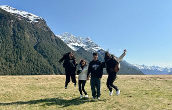 Four friends jumping in a green valley with snow-capped mountains