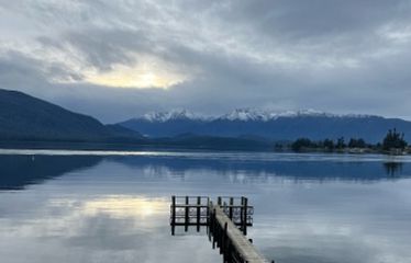 Wooden dock extending into a calm lake with mountains and clouds in the background
