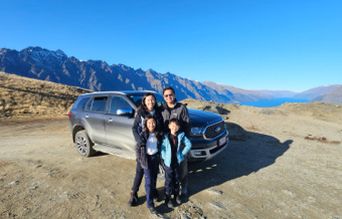 Family posing with an SUV on a scenic mountain road with a lake view