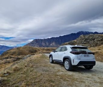 White GO Rentals SUV parked on a mountain trail with a backdrop of cloudy skies and hills