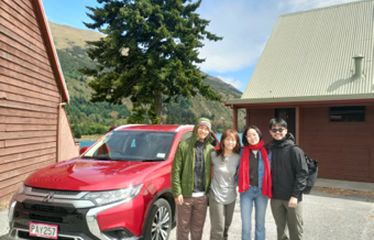 Four friends posing next to a red SUV in a scenic mountain lodge setting