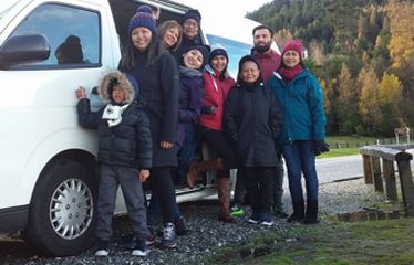 Group of people posing beside a white van in a scenic outdoor setting