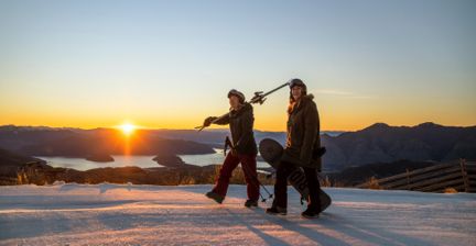 Two skiers walking at sunset with snow-covered peaks