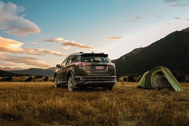 Image of a Toyota RAV4 at dusk parked next to a tent with mountains in the background