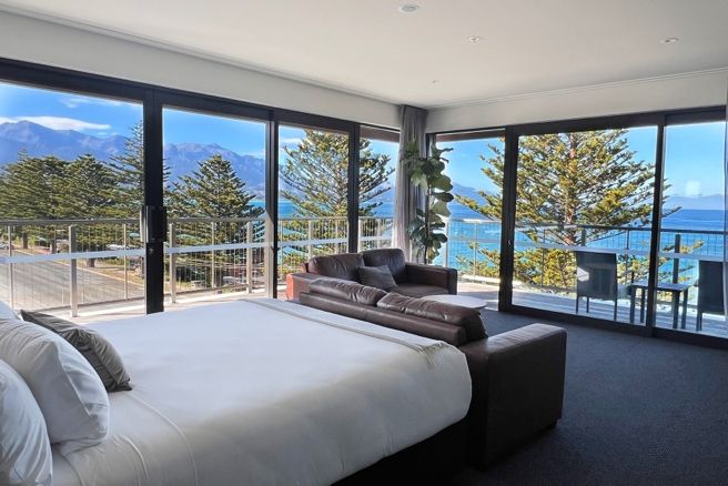 Spacious hotel room with large windows, ocean view, and mountain backdrop