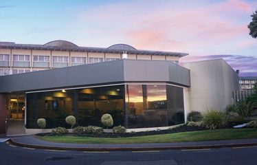 Sudima Rotorua hotel at sunset with curved glass-front building