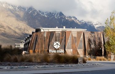 Sudima Queenstown hotel with mountains in the background and dry grass in front