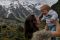 Image of a female holding up a baby and smiling with snowy mountains in the background