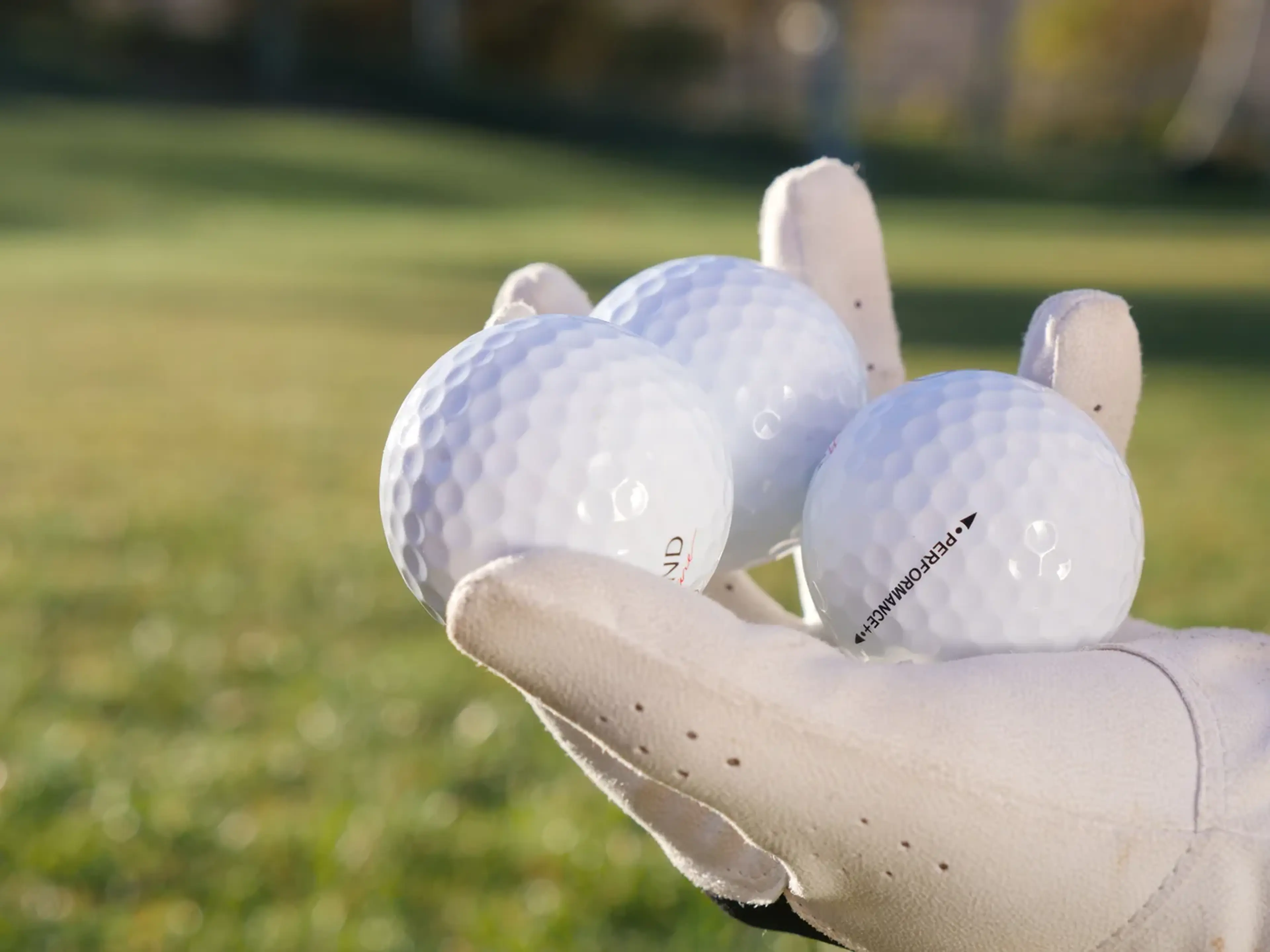 A gloved hand holding three golf balls