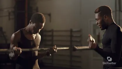 A trainer coaching a lifter through a barbell curl in a gym