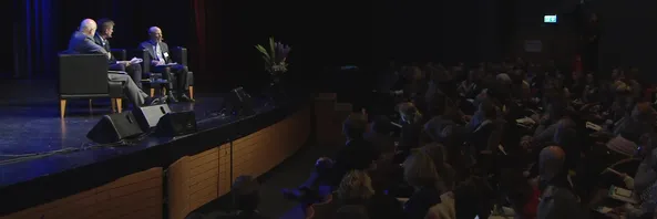Dr. Bruce Wampold on stage in conversation with two others, facing a full auditorium