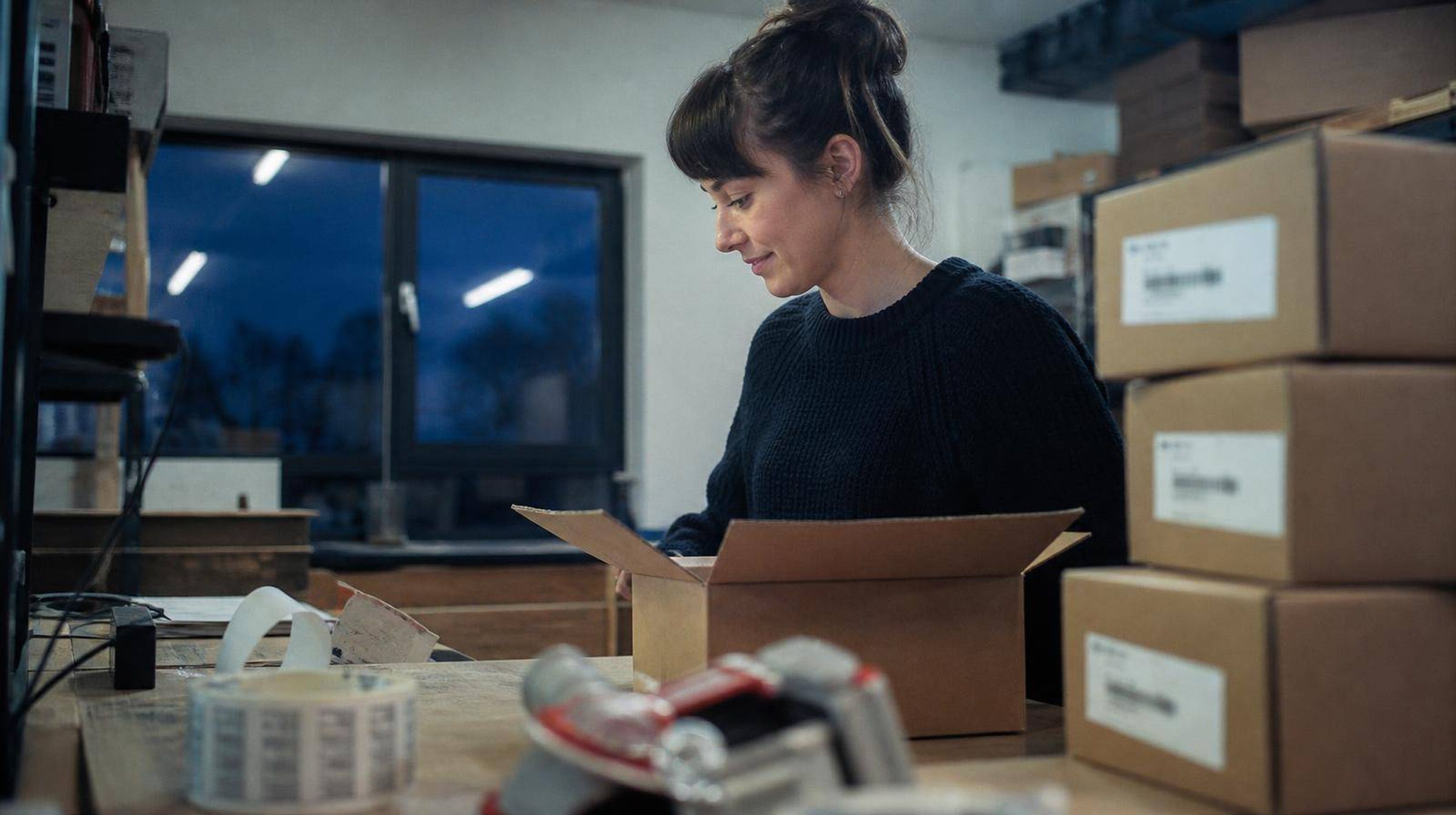 A packing bench with boxes part-filled, the owner taping the last orders