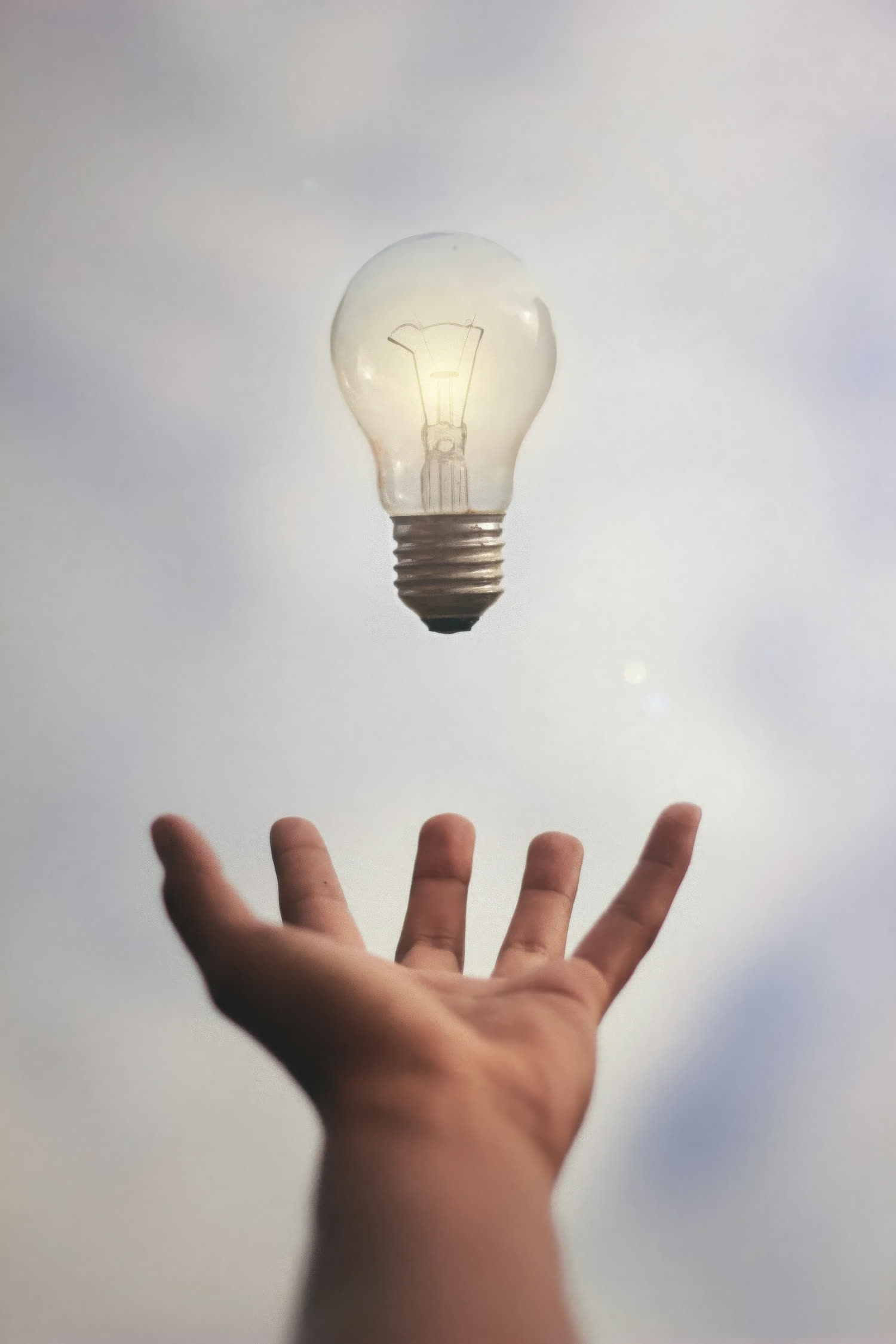 An open hand reaching towards a glowing lightbulb