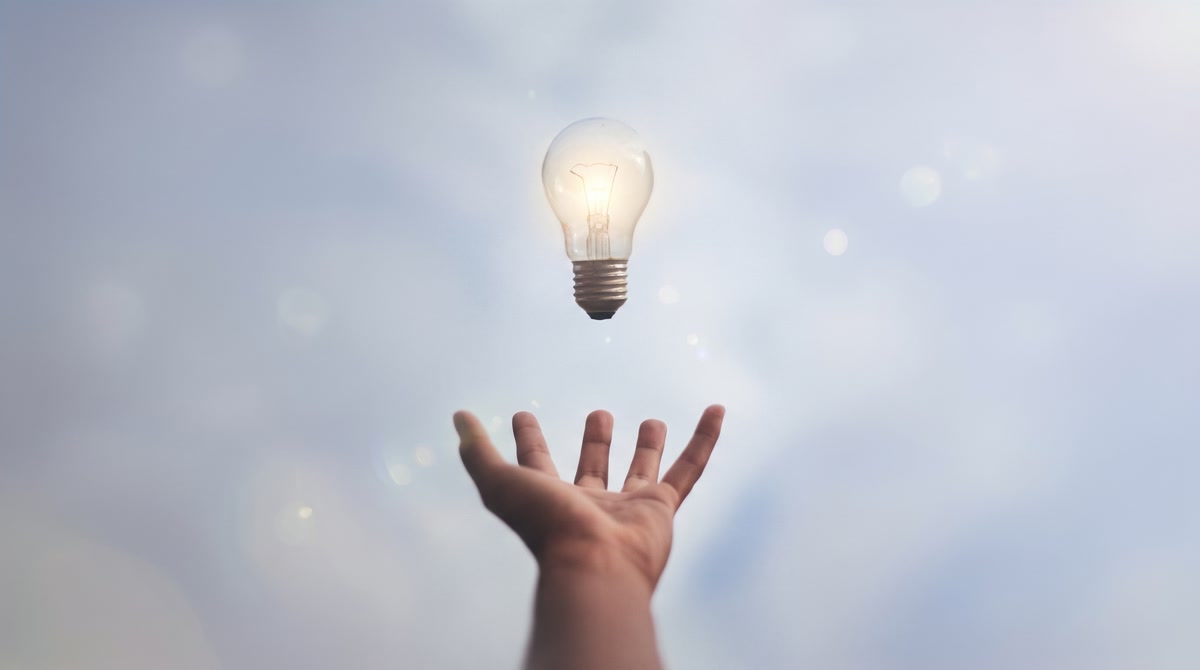 An open hand reaching towards a glowing lightbulb