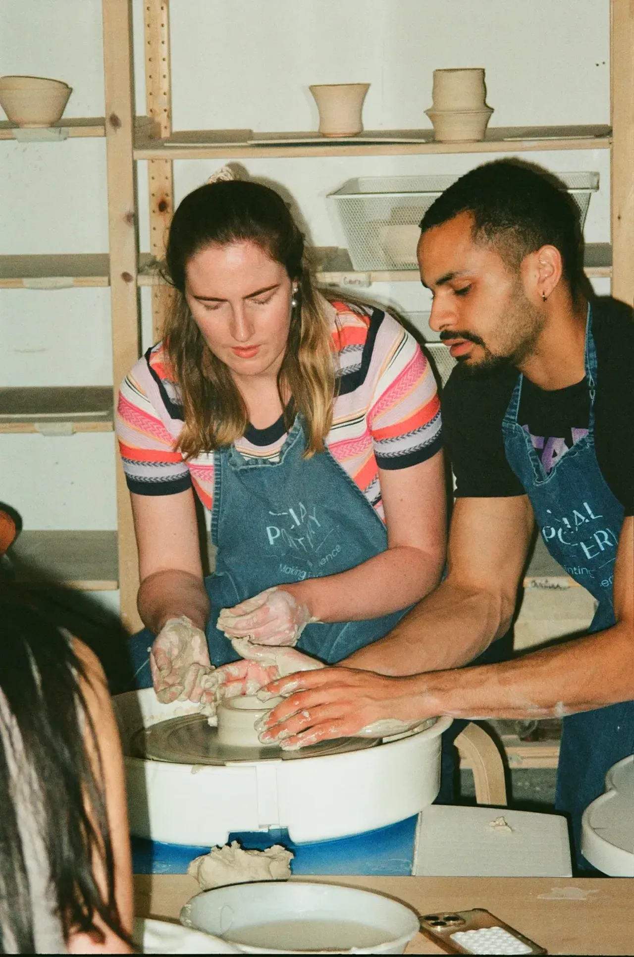 A tutor guiding a beginner’s hands at the pottery wheel