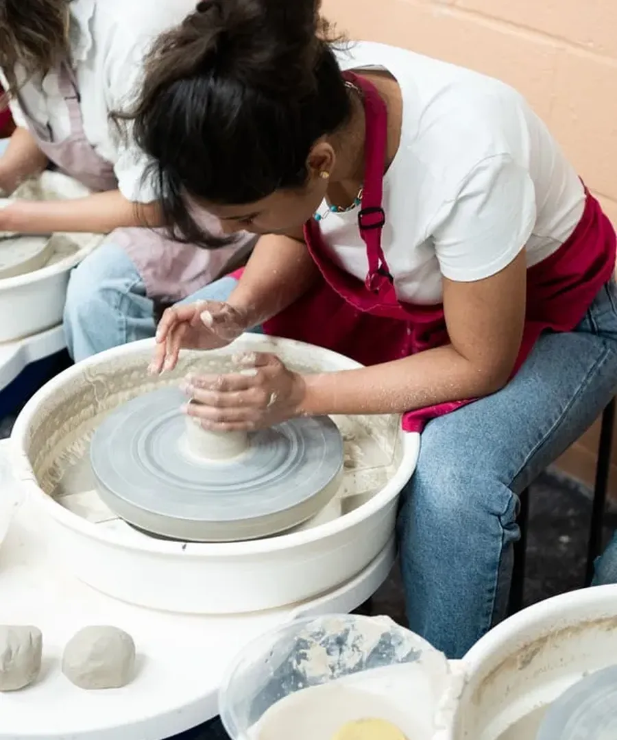 A beginner shaping a bowl on the pottery wheel during a Social Pottery class