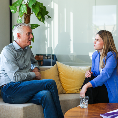 Een man en een vrouw zijn met elkaar in gesprek op een bank in een kantooromgeving