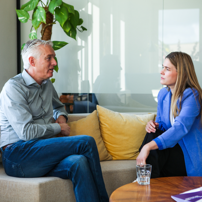 Een man en een vrouw zijn met elkaar in gesprek op een bank in een kantooromgeving
