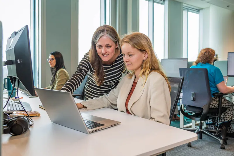 An Ace colleague looking over another’s shoulder at a laptop in the office